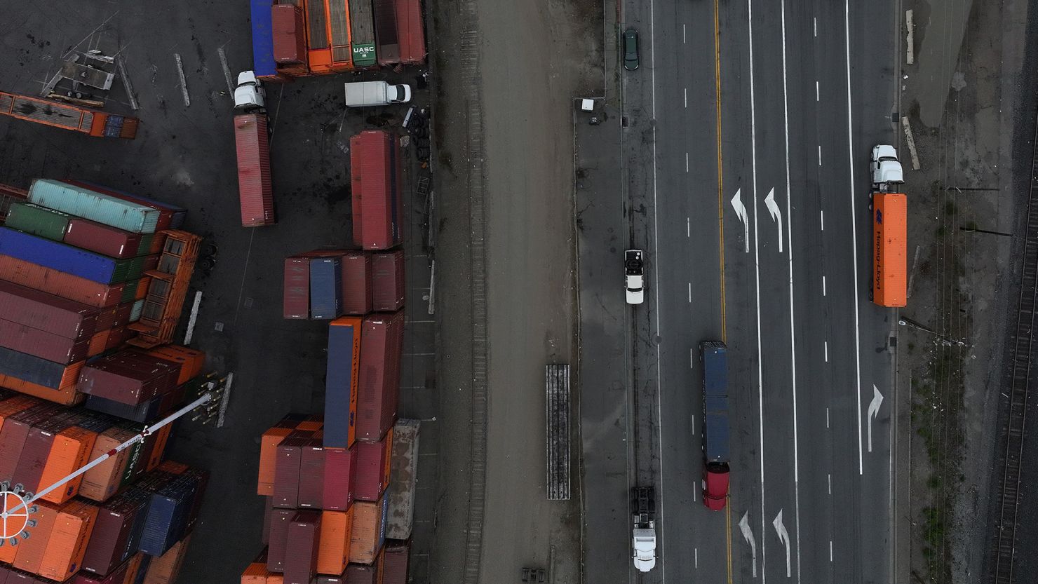 In an aerial view, trucks carrying shipping containers drive through the Port of Oakland.