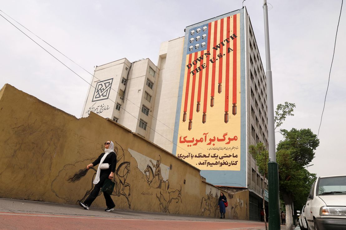 Women walk near a building bearing an anti-US mural with the slogan 