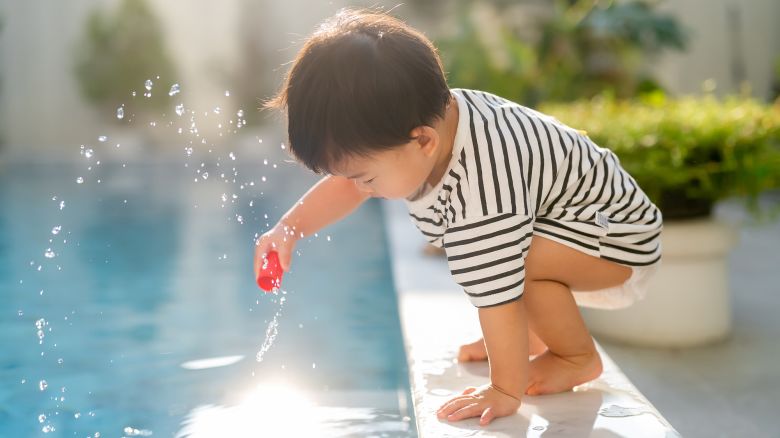 fun and cheerful Asian toddler child boy  sit over poolside and try to splash water with his hand summertime vacation playful moment