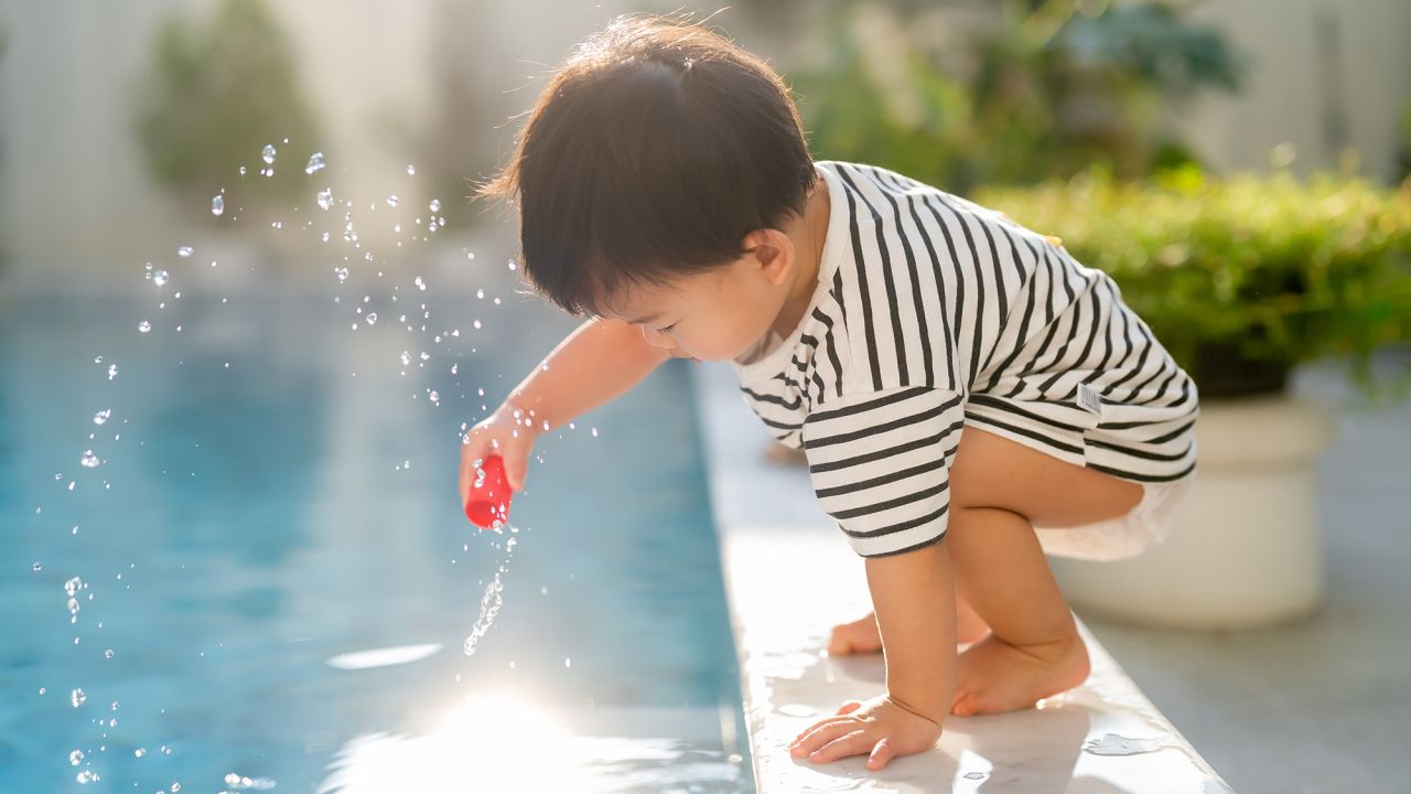 fun and cheerful Asian toddler child boy  sit over poolside and try to splash water with his hand summertime vacation playful moment