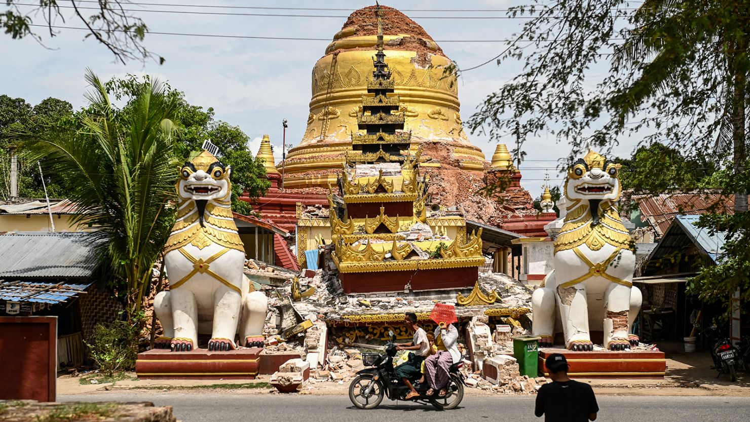 This photo taken on April 12, 2025 shows people driving past the debris of a damaged Buddha statue in Inwa on the outskirts of Mandalay, following the devastating March 28 earthquake.