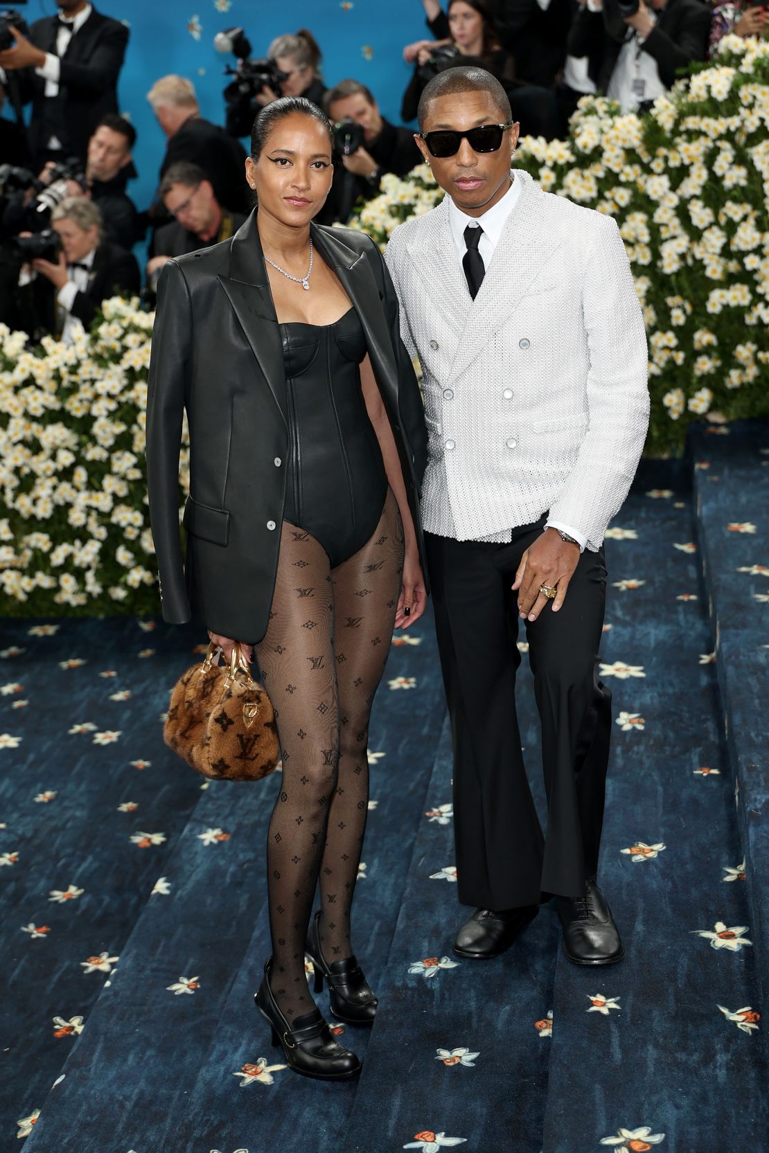 Pharrell Williams, who is serving as a co-chair of the event, wears a double-breasted Louis Vuitton blazer made of 15,000 pearls that took 400 hours to make, he noted. Helen Lasichanh, Williams’ wife, wears a corseted leather bodysuit and tights patterned with the logo of Louis Vuitton.