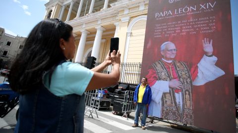 CHICLAYO, PERU - MAY 10: A person takes a photo as another person pose next to a LED screen depicting the image of newly elected Pope Leo XIV outside Chiclayo Cathedral on May 10, 2025 in Chiclayo, Peru. Leo XIV was elected by the Conclave on May 08 as the 267th pontiff. Born in Chicago on September 14, 1955 as Robert Francis Prevost, the current pope worked for many years in Peru before beIng named as bishop of Chiclayo from 2014 to 2023. (Photo by Raul Sifuentes/Getty Images
