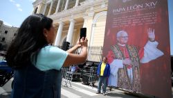 CHICLAYO, PERU - MAY 10: A person takes a photo as another person pose next to a LED screen depicting the image of newly elected Pope Leo XIV outside Chiclayo Cathedral on May 10, 2025 in Chiclayo, Peru. Leo XIV was elected by the Conclave on May 08 as the 267th pontiff. Born in Chicago on September 14, 1955 as Robert Francis Prevost, the current pope worked for many years in Peru before beIng named as bishop of Chiclayo from 2014 to 2023. (Photo by Raul Sifuentes/Getty Images