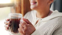 Home, hands and old woman with coffee, window view and morning routine with retirement. Apartment, mature person and senior lady in lounge, espresso and resting with break, smiling and closeup