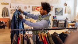 Young man arranging clothes on hangers in a vintage second-hand shop, creating an inviting display of unique garments for customers