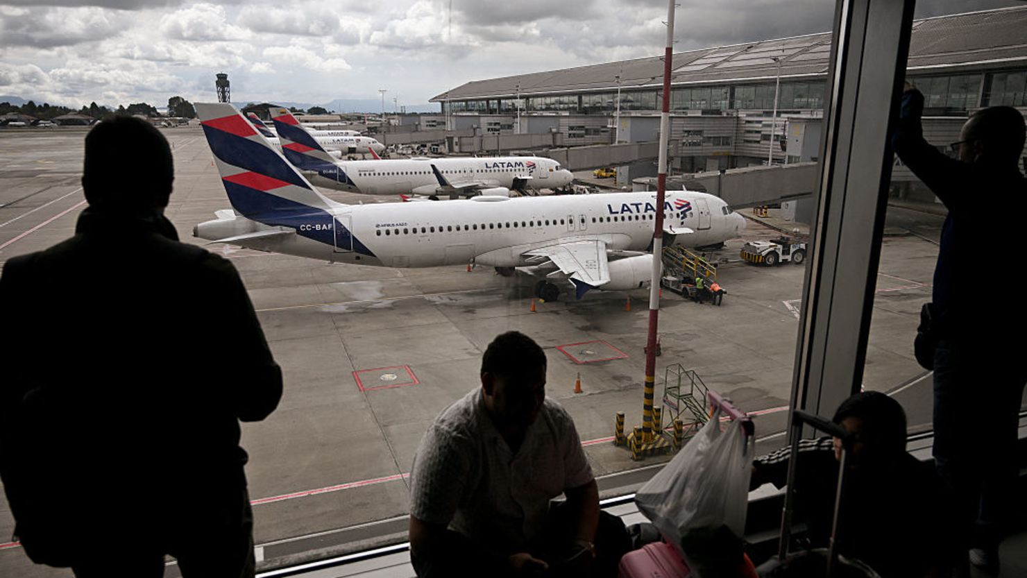 Pasajeros venezolanos observan los aviones de la aerolínea LATAM en la pista mientras esperan noticias tras la cancelación de su vuelo a Caracas en el Aeropuerto Internacional El Dorado de Bogotá el 19 de mayo de 2025.