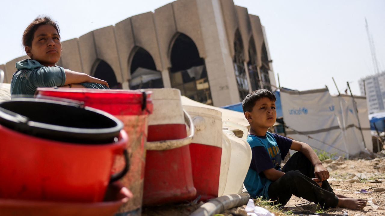 Children sit with plastic buckets as displaced Palestinians collect water in Gaza City, on May 20, 2025, amid the ongoing war between Israel and the Palestinian militant movement Hamas. Israel, pressing a newly expanded military offensive across the Gaza Strip, has faced mounting pressure including from key backer the United States to end the aid blockade it imposed on March 2. (Photo by Bashar TALEB / AFP) (Photo by BASHAR TALEB/AFP via Getty Images)