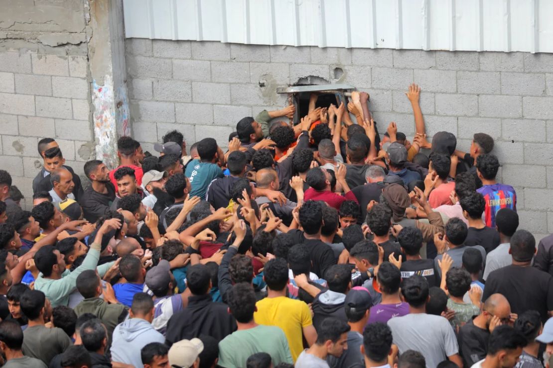 Palestinos desplazados tratan de alcanzar el pan que se distribuye a través de la ventana de una panadería en el campo de refugiados de Nusseirat el jueves.