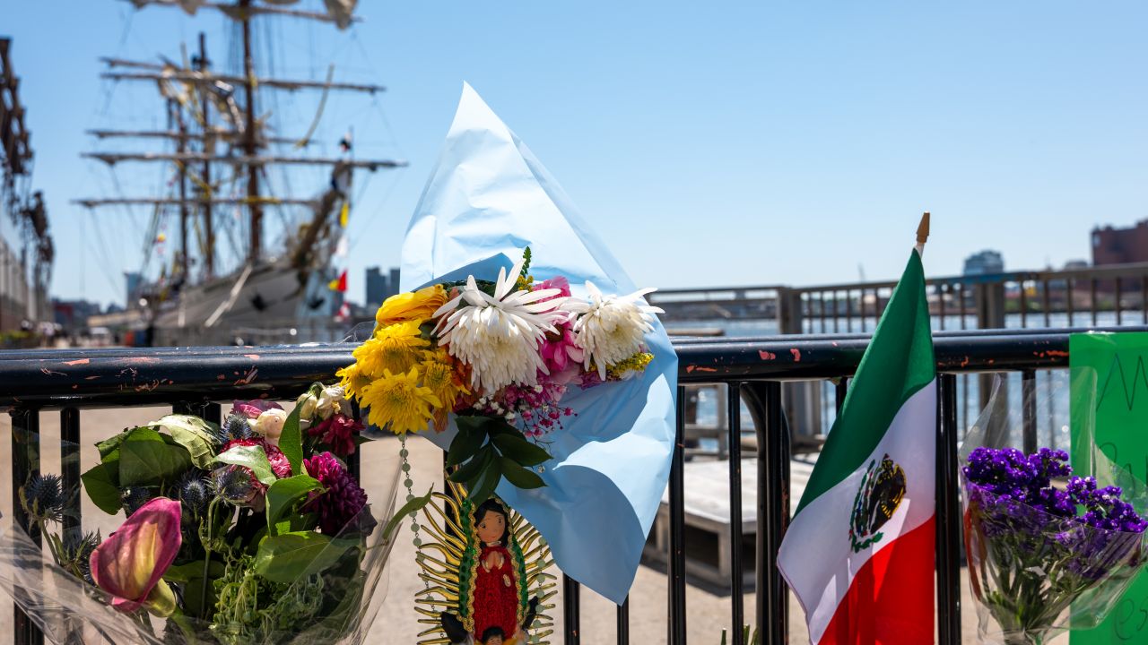 NEW YORK, NEW YORK - MAY 19: Flowers and flags are placed on a gate by a damaged Mexican Navy sailing ship, the Cuauhtémoc, that crashed into the Brooklyn Bridge over the weekend in lower Manhattan on May 19, 2025 in New York City. The collision, which snapped all three of the masts on the ship as it collided with the landmark bridge, killed at least two crew members and injured 19 others. (Photo by Spencer Platt/Getty Images)