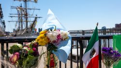 NEW YORK, NEW YORK - MAY 19: Flowers and flags are placed on a gate by a damaged Mexican Navy sailing ship, the Cuauhtémoc, that crashed into the Brooklyn Bridge over the weekend in lower Manhattan on May 19, 2025 in New York City. The collision, which snapped all three of the masts on the ship as it collided with the landmark bridge, killed at least two crew members and injured 19 others. (Photo by Spencer Platt/Getty Images)