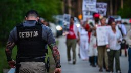Un funcionario de prisiones camina junto a personas que portan velas, carteles y flores durante una vigilia frente al Centro de Detención Krome en Miami el 24 de mayo de 2025. Imagen ilustrativa.