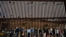 People lay their hands on the border wall and pray towards Mexico during Pastor Seth Clark's last service for The Border Church at the stretch of the US-Mexico border fence known as "Whiskey 8" in San Diego, California on May 25, 2025. As pastor Seth Clark retires from his leadership role with The Border Church the mission of the interdenominational Christian ministry to maintain presence and sacramental solidarity appears more challenging now than ever. While weekly binational communion services started in 2011 on both sides of the US and Mexico border, the US side of the International Friendship Park has remained closed since February 2020 with fears it will never reopen. The recent addition of concertina wire along the top and bottom of the border wall bollards features sharp barbs akin to a crown of thorns meant to deter migrant crossings. (Photo by Patrick T. Fallon / AFP) (Photo by PATRICK T. FALLON/AFP via Getty Images)          