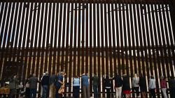 People lay their hands on the border wall and pray towards Mexico during Pastor Seth Clark's last service for The Border Church at the stretch of the US-Mexico border fence known as "Whiskey 8" in San Diego, California on May 25, 2025. As pastor Seth Clark retires from his leadership role with The Border Church the mission of the interdenominational Christian ministry to maintain presence and sacramental solidarity appears more challenging now than ever. While weekly binational communion services started in 2011 on both sides of the US and Mexico border, the US side of the International Friendship Park has remained closed since February 2020 with fears it will never reopen. The recent addition of concertina wire along the top and bottom of the border wall bollards features sharp barbs akin to a crown of thorns meant to deter migrant crossings. (Photo by Patrick T. Fallon / AFP) (Photo by PATRICK T. FALLON/AFP via Getty Images)          