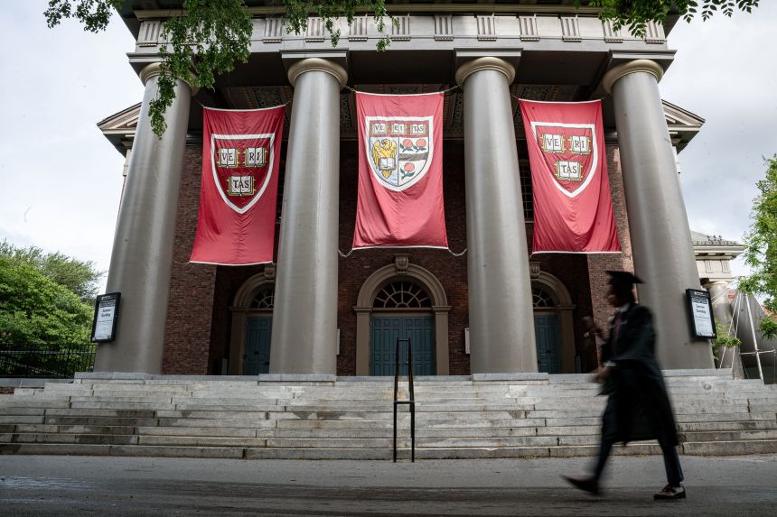 A person in cap and gown walks Saturday on Harvard University's campus in Cambridge, Massachusetts.