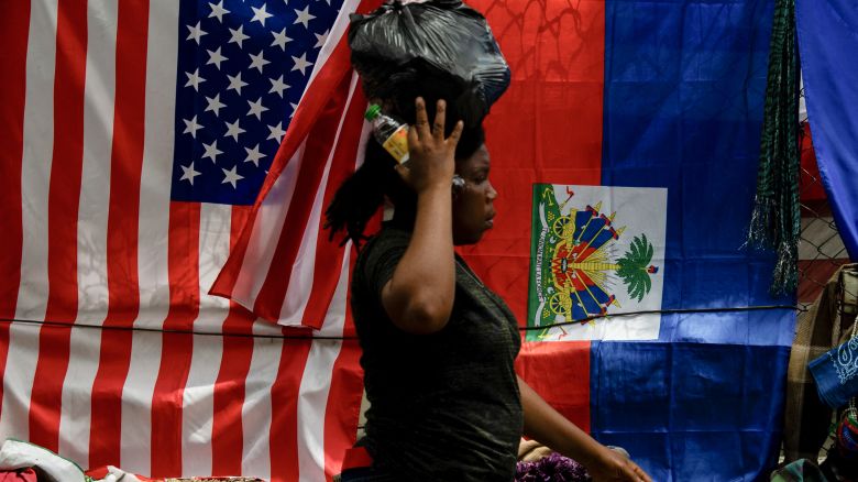 A woman walks past a vendor's stall next to US and Haitian flags displayed for sale along with scarves and crafts in Port-au-Prince, Haiti, on June 6, 2025. US President Donald Trump's inclusion of Haiti in his istration's list of countries that are banned from travel visas has hit the Caribbean nation struggling with gang violence hard, both there and among its expats. (Photo by Clarens SIFFROY / AFP) (Photo by CLARENS SIFFROY/AFP via Getty Images)          