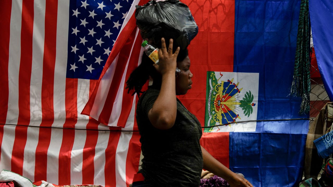 A woman walks past a vendor's stall next to US and Haitian flags displayed for sale along with scarves and crafts in Port-au-Prince, Haiti, on June 6, 2025. US President Donald Trump's inclusion of Haiti in his istration's list of countries that are banned from travel visas has hit the Caribbean nation struggling with gang violence hard, both there and among its expats. (Photo by Clarens SIFFROY / AFP) (Photo by CLARENS SIFFROY/AFP via Getty Images)          