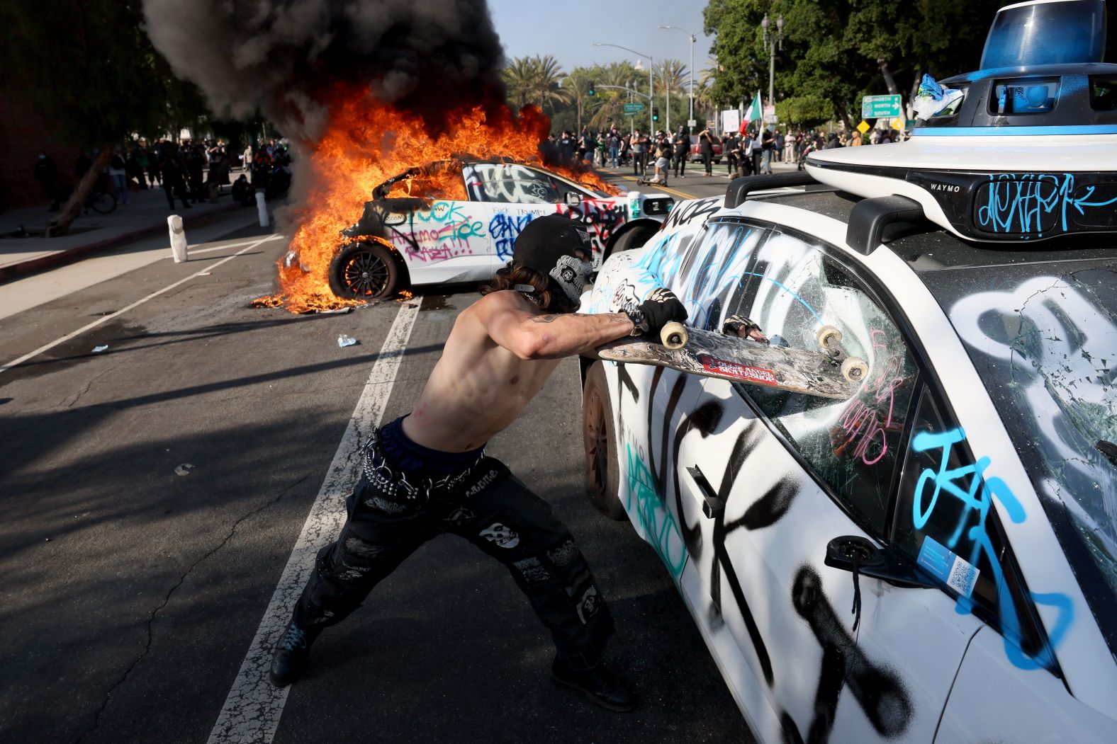 A protester damages a self-driving Waymo vehicle at Los Angeles St. and Arcadia in Los Angeles on Sunday.