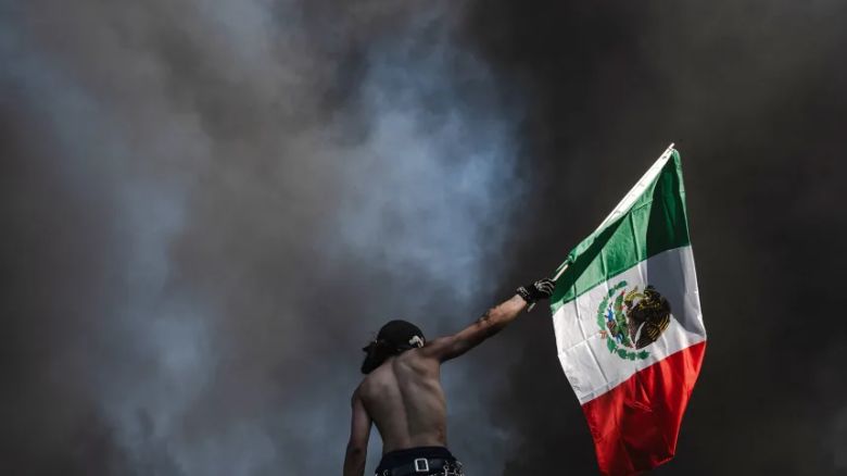 Un manifestante ondea una bandera mexicana frente a la columna de humo que emana de autos en llamas el domingo en el centro de Los Ángeles.