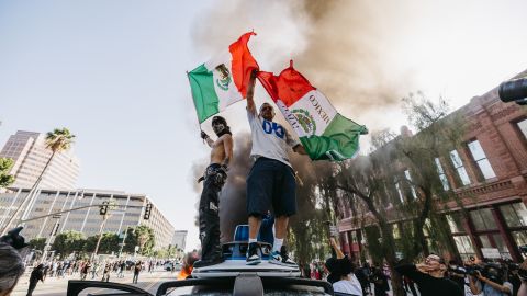 Two protesters wave Mexican flags while standing on a vandalized Waymo vehicle during a demonstration in Los Angeles, California, on June 8, 2025. Following a series of aggressive federal immigration operations in Los Angeles, tensions escalated when Immigration and Customs Enforcement (ICE) agents conducted a high-profile raid on a Home Depot location. The raid sparked widespread protests across the city, where demonstrators decried the targeting of immigrant communities and the separation of families. Clashes soon broke out between protesters and federal agents, prompting U.S. President Donald Trump to deploy 2,000 National Guard troops to the city, a move harshly criticized by California officials, including the governor, as "purposefully inflammatory." (Photo by David Pashaee / Middle East Images via AFP) (Photo by DAVID PASHAEE/Middle East Images/AFP via Getty Images)