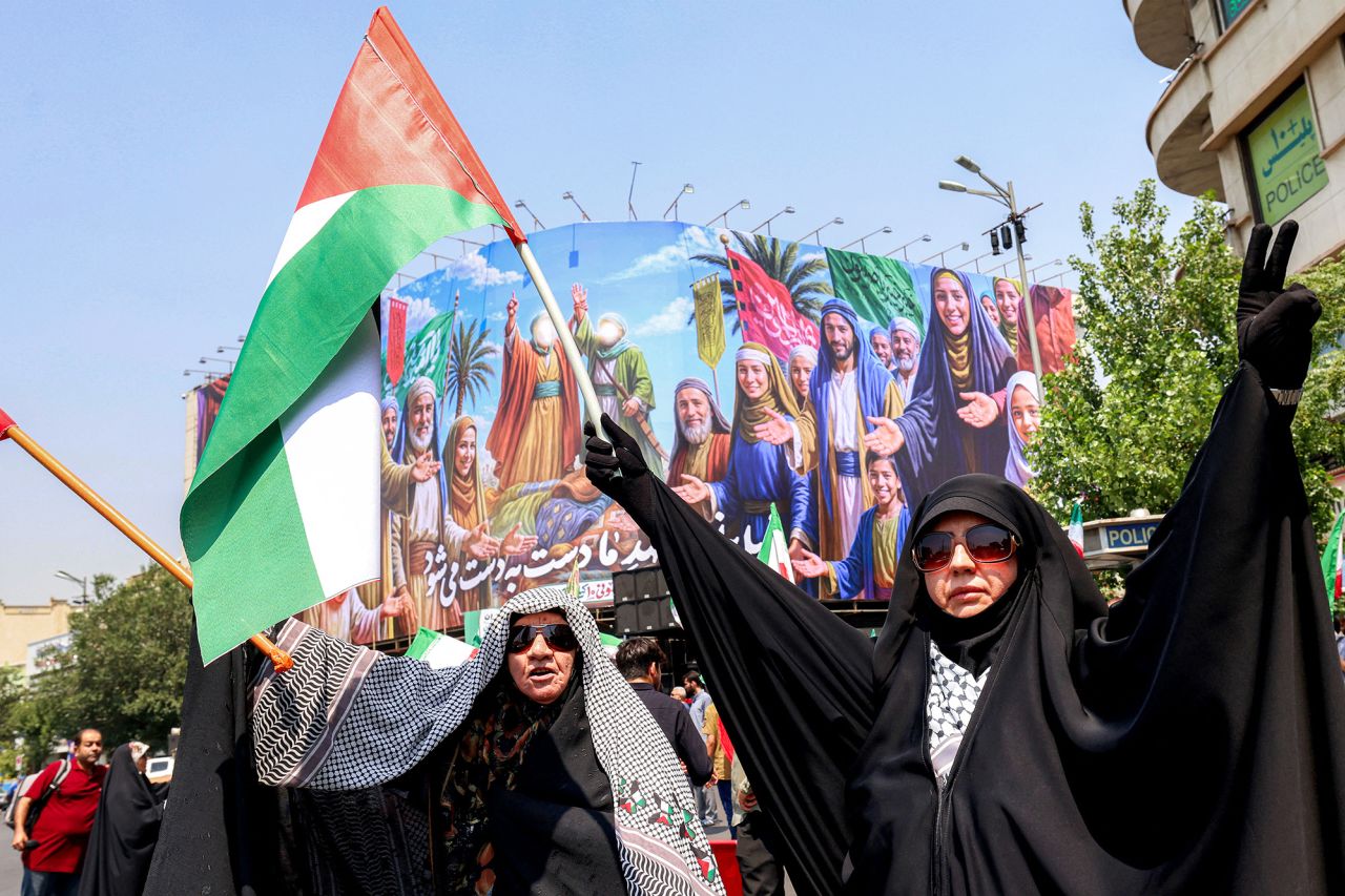 A woman holds a Palestinian flag and another an Iranian flag as people gather for a protest against Israel's wave of strikes on Iran in Enghelab Square in central Tehran on Friday.