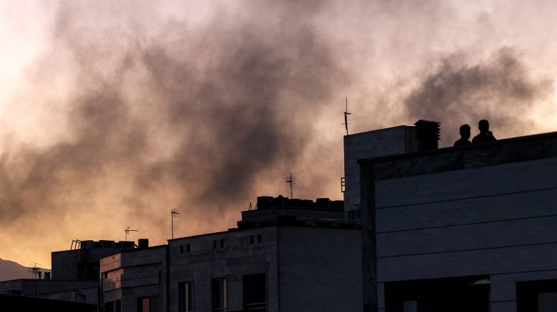 People stand on a rooftop amidst billowing smoke following an overnight Israeli strike in Tehran on June 17.