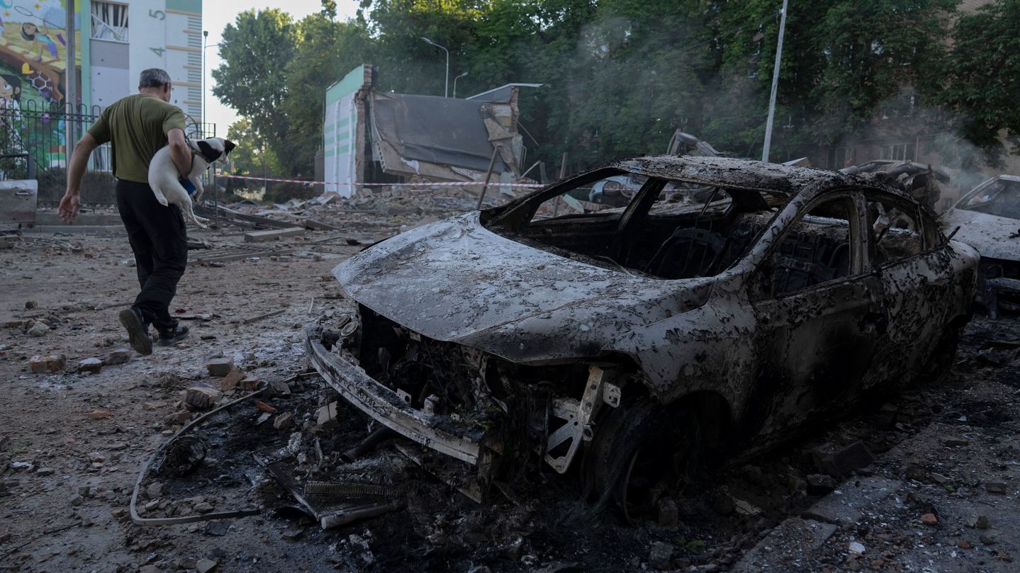 A man carrying a dog walks past the wreckage of cars following mass Russian drones and missile strike on the Ukraine's capital Kyiv on July 4, 2025, amid the Russian invasion of Ukraine. Kyiv said on July 4 that Russia had launched its largest overnight aerial attack on Ukraine over the more than three-year invasion. A representative of Ukraine's air force Yuriy Ignat said the barrage of 550 drones and missiles was a record, adding "this is the largest number that the enemy has used in a single attack." (Photo by OLEKSII FILIPPOV / AFP) (Photo by OLEKSII FILIPPOV/AFP via Getty Images)