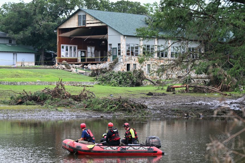 A search and rescue team floats Monday along the Guadalupe River past a damaged building at Camp Mystic in Hunt, Texas.