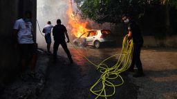 Police officers try to extinguish a car on fire in L'Estaque a district of Marseille, southern France on July 8, 2025, as the smoke from a wildfire rises. The fire that started late on July 8, 2025 morning in Les Pennes-Mirabeau (Bouches-du-Rhone), a town bordering Marseille, has entered France's second-largest city, where some residents were urged to shelter in place, according to a warning message at 4:00 PM from the prefect of Bouches-du-Rhone. (Photo by Clement MAHOUDEAU / AFP) (Photo by CLEMENT MAHOUDEAU/AFP via Getty Images)          