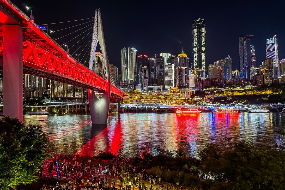 Tourists gather along the riverside promenade near the illuminated Qiansimen Bridge. (Photo by Cheng Xin/Getty Images)