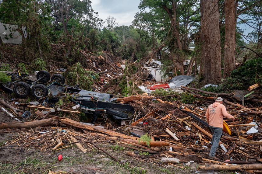A volunteer walks through debris while assisting with search and rescue efforts on the banks of the Guadalupe River in Center Point, Texas.