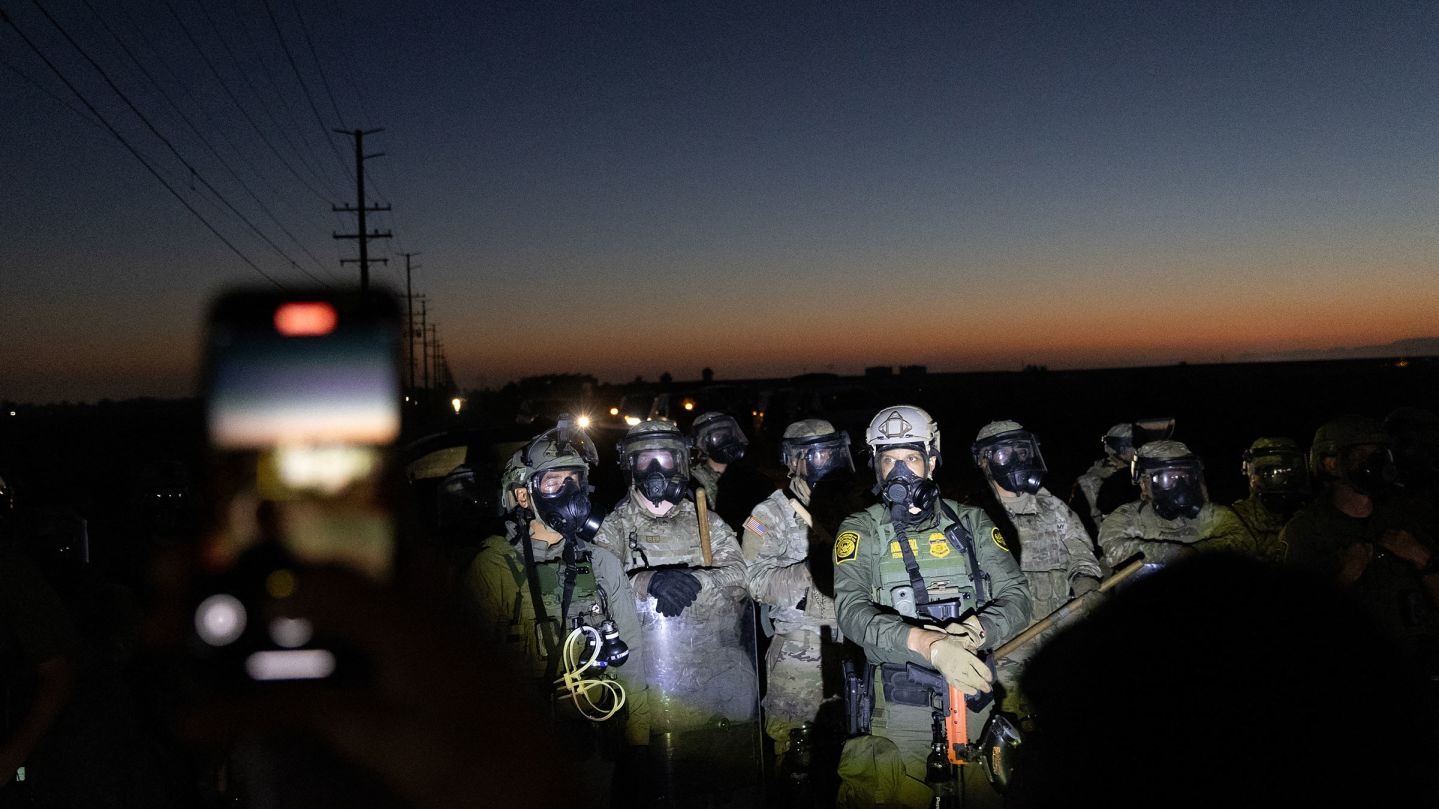 Customs and Border Protection officers and California National Guard troops hold the line as protestors shine flashlights on them after Federal Immigration agents conducted a raid on Glass House Farms in Camarillo, California, on July 10, 2025. Federal immigration agentsbacked by CBP, Border Patrol units, National Guard troops, helicopters, and military style vehiclesraided Glass House Farms in Camarillo early July 10, 2025, targeting state licensed cannabis and other crop operations, detaining between a dozen and 100 farmworkers, and deploying smoke or tear gas canisters and rubber bullets to disperse a crowd of several hundred protesters on Laguna Road. (Photo by BLAKE FAGAN / AFP) (Photo by BLAKE FAGAN/AFP via Getty Images)          