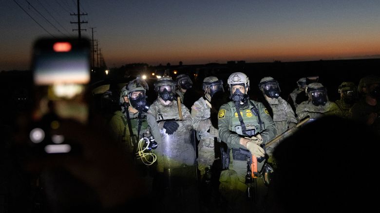 Customs and Border Protection officers and California National Guard troops hold the line as protestors shine flashlights on them after Federal Immigration agents conducted a raid on Glass House Farms in Camarillo, California, on July 10, 2025. Federal immigration agentsbacked by CBP, Border Patrol units, National Guard troops, helicopters, and military style vehiclesraided Glass House Farms in Camarillo early July 10, 2025, targeting state licensed cannabis and other crop operations, detaining between a dozen and 100 farmworkers, and deploying smoke or tear gas canisters and rubber bullets to disperse a crowd of several hundred protesters on Laguna Road. (Photo by BLAKE FAGAN / AFP) (Photo by BLAKE FAGAN/AFP via Getty Images)          