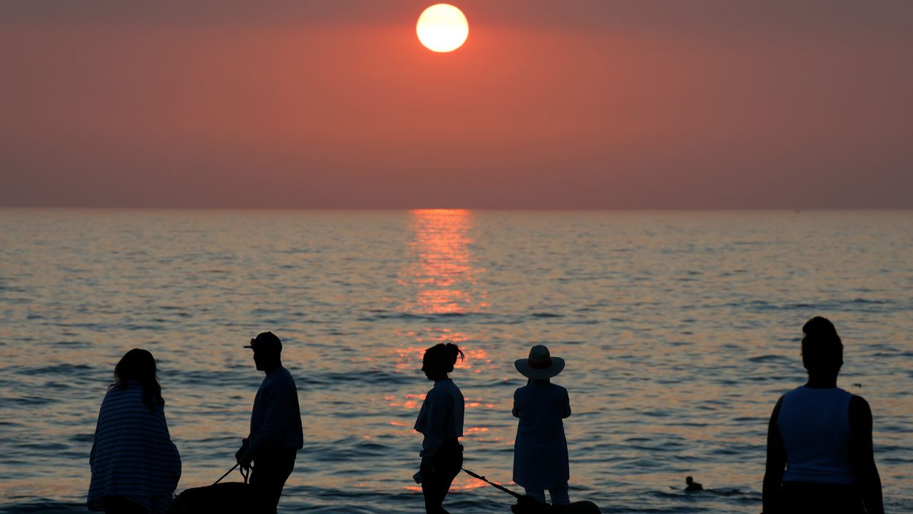 People gather along the La Jolla coastline as the sun sets on the horizon of the Pacific Ocean while smoke from Southern California wildfires fills the air on August 5, 2025 in San Diego, California.
