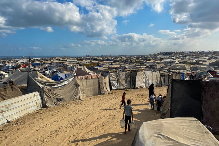 Palestinian children carry water jugs past tents, housing displaced people, in the Mawasi area in Khan Younis in the southern Gaza Strip on August 7.
