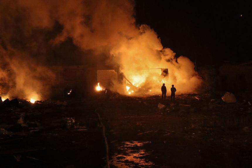 People stand in front of burning building in Okhtyrka, Ukraine, after Russian drone attack on Wednesday.