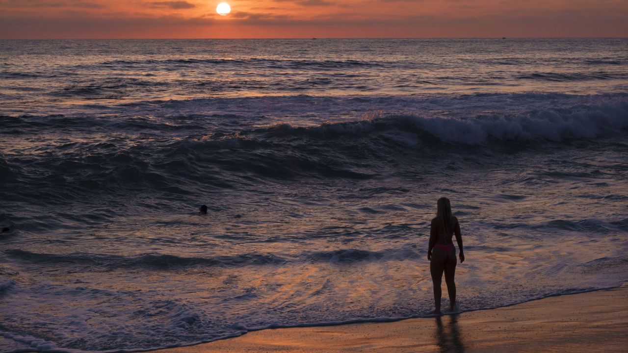A woman watches the Pacific Ocean at La Jolla's Windansea Beach at sunset during a summer heat wave on August 24, 2025 in San Diego, California.