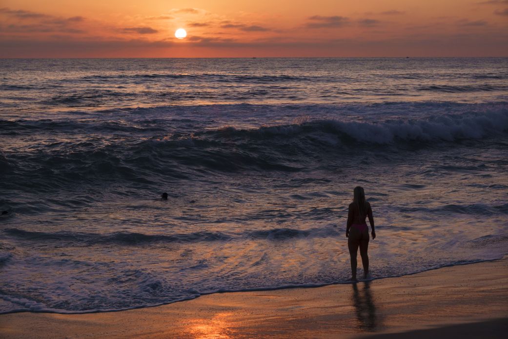 A woman watches the sunset over the Pacific Ocean at La Jolla's Windansea Beach during a summer heat wave on August 24, in San Diego, California.