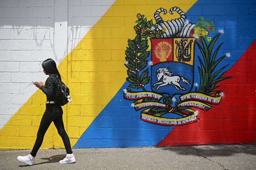 A woman walks in front of a mural with the Venezuelan coat of arms in Caracas on September 1.