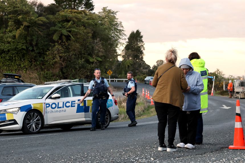Police officers and locals stand near a roadblock where a police shootout occurred near the town of Piopio, located in New Zealand's Waikato region on September 8, 2025.