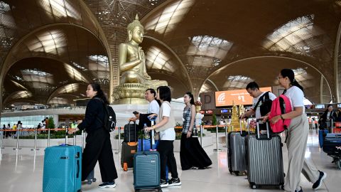 Passengers walk with their luggage past a statue of Buddha on the inauguration day of the newly built Techo International Airport in Kandal province, on the outskirts of Phnom Penh, on September 9, 2025. A new major airport serving the capital Phnom Penh began operations. (Photo by TANG CHHIN Sothy / AFP) (Photo by TANG CHHIN SOTHY/AFP via Getty Images)          