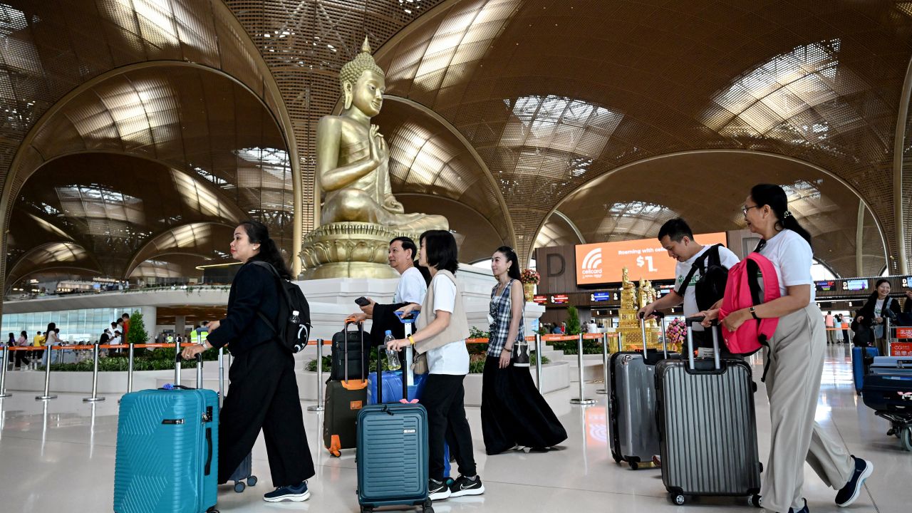 Passengers walk with their luggage past a statue of Buddha on the inauguration day of the newly built Techo International Airport in Kandal province, on the outskirts of Phnom Penh, on September 9, 2025. A new major airport serving the capital Phnom Penh began operations. (Photo by TANG CHHIN Sothy / AFP) (Photo by TANG CHHIN SOTHY/AFP via Getty Images)          