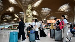 Passengers walk with their luggage past a statue of Buddha on the inauguration day of the newly built Techo International Airport in Kandal province, on the outskirts of Phnom Penh, on September 9, 2025. A new major airport serving the capital Phnom Penh began operations. (Photo by TANG CHHIN Sothy / AFP) (Photo by TANG CHHIN SOTHY/AFP via Getty Images)          