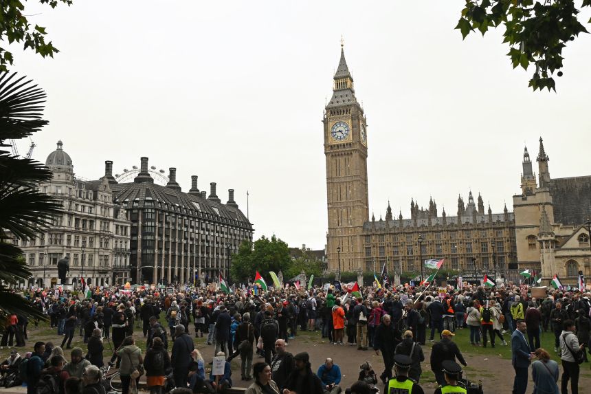 Protesters carry placards and Palestinian flags that gather on Wednesday in Parliament Square along with Parliamentary House in London background.