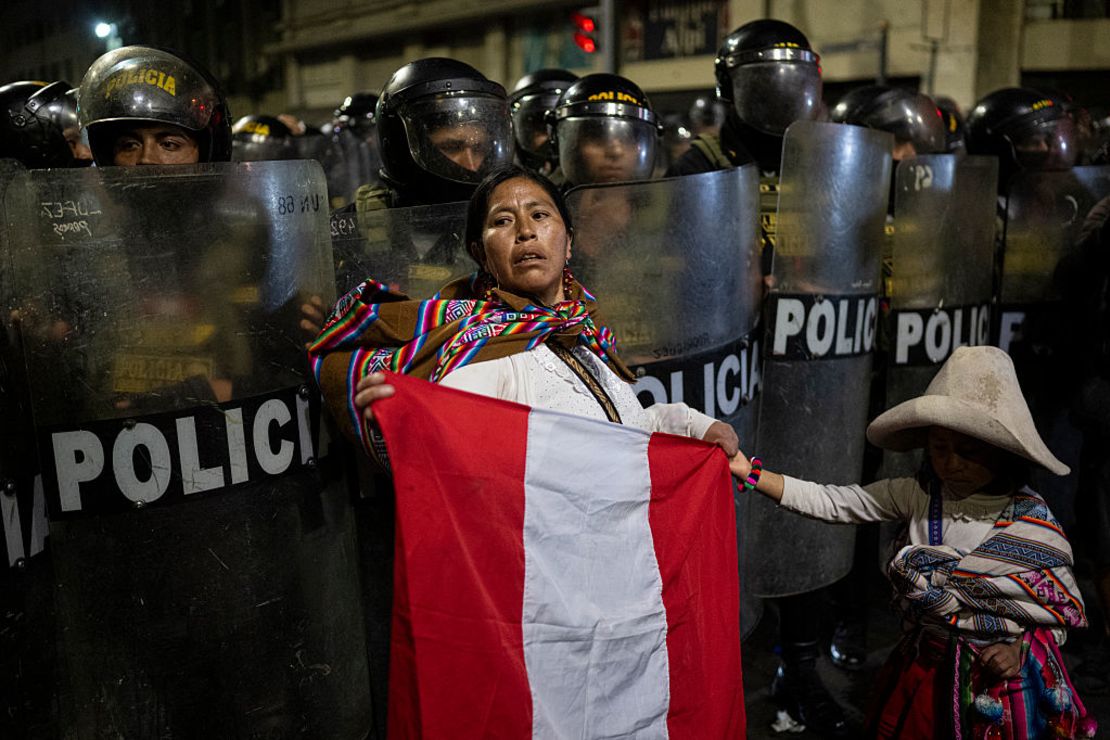 Una mujer indígena con un niño sostiene una bandera peruana frente a la policía antidisturbios durante una manifestación en Lima el 21 de septiembre de 2025.