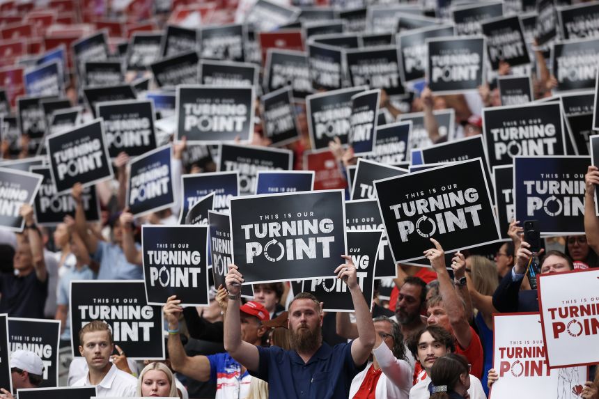 Attendees hold up Turning Point USA signs at the memorial service for political activist Charlie Kirk at State Farm Stadium on September 21, 2025 in Glendale, Arizona.
