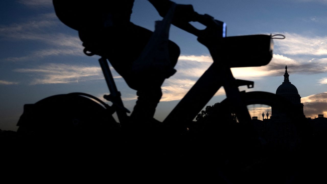 The US Capitol building is seen in the background as a man rides a bike along the street on October 1, 2025.