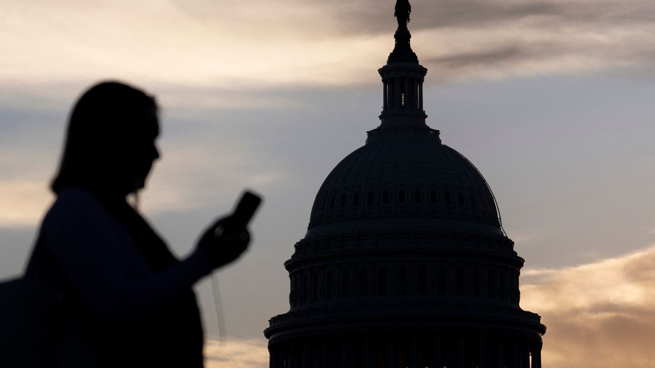 A woman looks at her phone while walking past the US Capitol building on the first day of the government shutdown October 1, 2025, in Washington, DC. The US government began shutting down after midnight on October 1 as lawmakers and President Donald Trump failed to break a budget impasse during acrimonious talks that hinged on Democratic demands for health care funding.