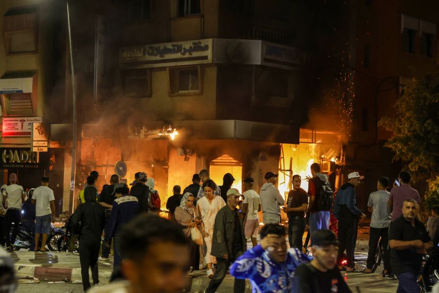 Moroccans pass by a bank building set on fire during a youth-led demonstration demanding widespread reforms across the education and healthcare sector in the northwestern city of Sale on October 1.