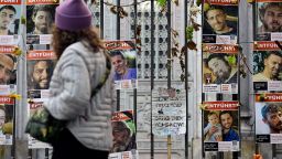 A woman passes a placard with the lettering 'Bring them home now' that is seen among portraits of hostages and victims of Palestinian militant group Hamas that are attached to the fence of the New Synagogue in Berlin on October 6, 2025, one day before the second anniversary of Hamas's October 7, 2023 attack on Israel. Delegations from Hamas, Israel and the United States are due to convene in Egypt for talks on October 6, with US President Trump urging negotiators to "move fast" to end the nearly two-year war in Gaza. Both Hamas and Israel have responded positively to Trump's proposal for an end to the fighting and the release of captives in Gaza in exchange for Palestinians held in Israeli jails. (Photo by John MACDOUGALL / AFP) (Photo by JOHN MACDOUGALL/AFP via Getty Images)          